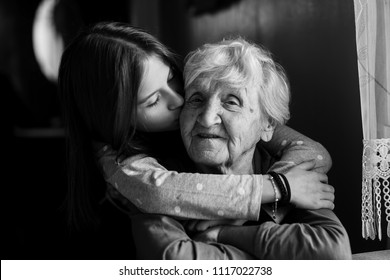 A Little Girl Hugs Her Grandmother. Black And White Photo.