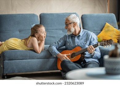 Little girl impressed by her grandfather playing guitar and making a surprised face - Powered by Shutterstock