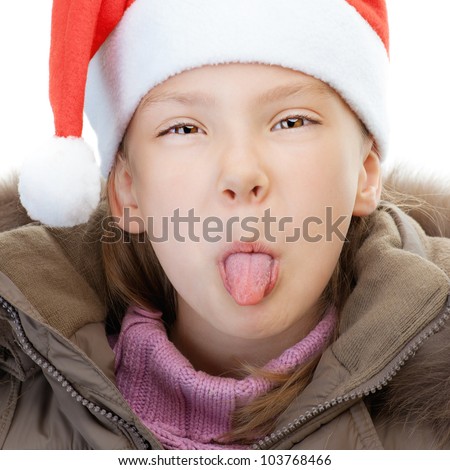 Little girl in jacket and Christmas hat show tongue, isolated on white background.
