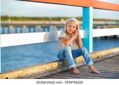 A little girl in jeans and a T-shirt sits on a pier near the Baltic Sea.Palanga, Lithuania