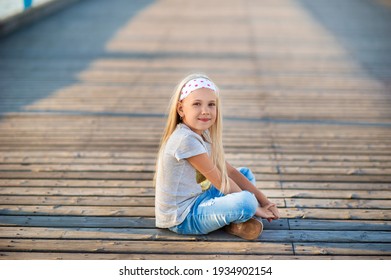 A little girl in jeans and a T-shirt sits on a pier near the Baltic Sea.Palanga, Lithuania.