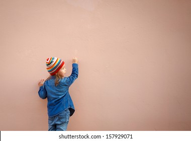 Little Girl In Jeans Writing On The Wall. Empty Space For Text Or Draw.