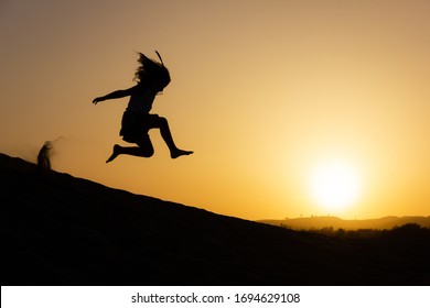 Little girl jumping over sand dunes on sunset in Maspalomas, Gran Canaria. Brave kid silhouette in the air at twilight in Canary Islands, Spain. No fear, courage, dare concepts