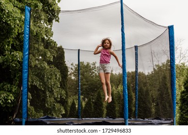 Little girl jumping in trampoline outdoors on an overcast day.