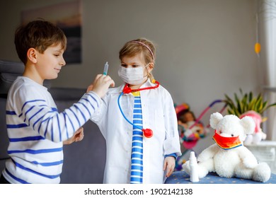 Little Girl And Kid Boy Makes Injection To Teddy Bear. Children, Siblings With Medical Mask Playing Doctor, Holding Syringe With Vaccine. Coronavirus Covid Vaccination Concept. Kids Play Role Game