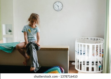 Little Girl Kid Getting Dressed By Herself, Going To Kindergarten In The Morning. Clock On The Wall In Bedroom 