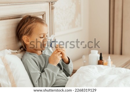 Little girl kid making inhalation with nebulizer at home at bed. child asthma inhaler inhalation steam sick pacient inhaling through inhaler mask. Self treatment of the respiratory tract