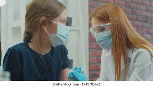 Little Girl Kid In Protective Medical Mask Is Getting Vaccinated. Female Doctor Injects Vaccine Into Child's Shoulder.