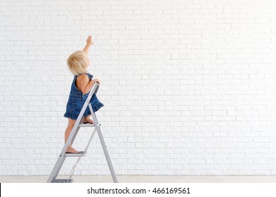 Little girl at the ladder, with the white brick wall on background.