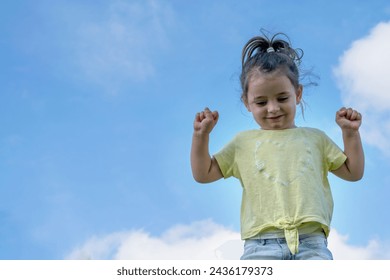 A little girl laughs with her arms raised under the bright summer sunher infectious laughter filling the air as the blue sky creates a perfect backdrop for this scene of pure joy and childlike happine