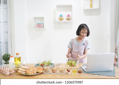 Little Girl Learning Online Cooking With Using Laptop Computer In The Kitchen At Home  