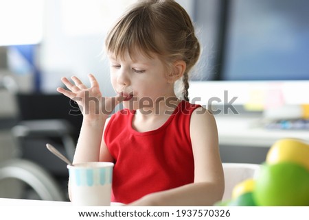 Little girl licking her fingers in front of glass of ice cream
