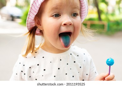 Little Girl Licking Lollypops And Showing Colored Blue Tongue. Concept Of Food Coloring In Children's Sweets, Artificial Food Dyes, Natural Dyes, Food Coloring Allergies