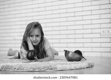 little girl lies on the floor and eats an apple