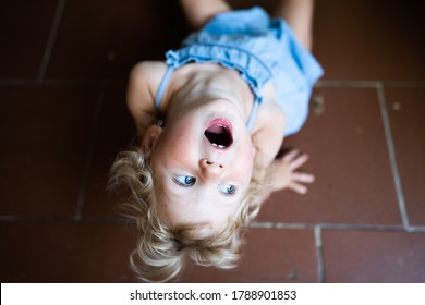 Little Girl Lies On Ground With Open Mouth