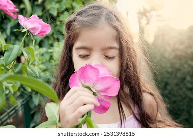 A little girl with long hair gently smells a pink rose in a sunlit garden, her eyes closed in a moment of peace and connection with nature - Powered by Shutterstock