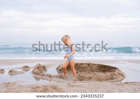 Little girl with long hair playing with sand on beach building castle at Mediterranean seaside in Spain. Carefree childhood, happiness concept.