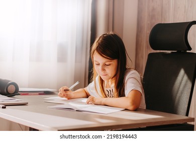 Little Girl With Long Hairs Sitting At Table, Holding Pen, Writing, Learning At Home. Teenager Studying Indoors At Room With Modern Black Chair. Home Education