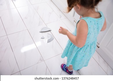 Little Girl Looking At Broken White Plate In Kitchen