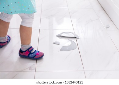 Little Girl Looking At Broken White Plate In Kitchen