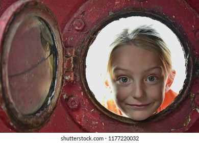 Little girl looking out of a old porthole.