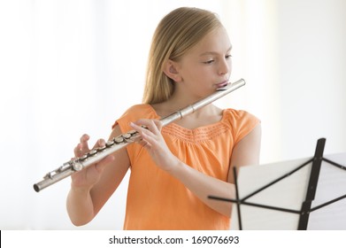 Little girl looking at sheet music while practicing flute at home