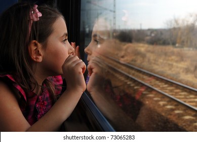 Little girl looking through window. She travels on a train.