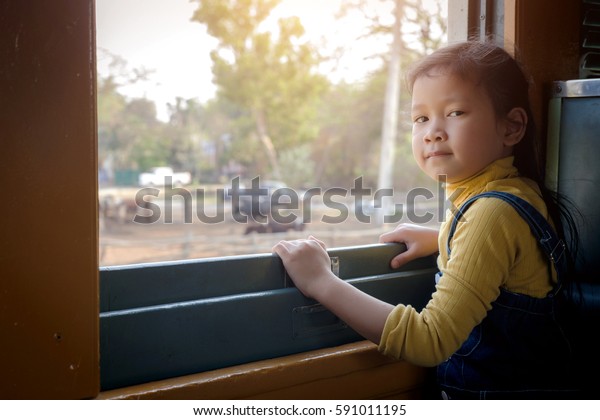   Little girl looking\
through window. She travels on a train.Girl looking out the train\
window.