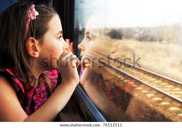 Little girl looking through window. She travels on\
a train.