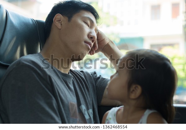 Little girl looks at her tired dad while he\'s\
sleeping on the bus