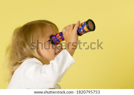 A little girl looks into a telescope or in a kaleidoscope.