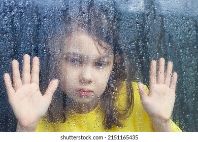 A Little Girl Looks Out Of A Rainy Window. A Little Girl Is Sad Looking Out Of A Rainy Window