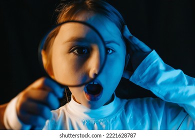 A Little Girl Looks Through A Magnifying Glass. Different Emotions Of The Child. The Book Is In The Hands Of A Child. The Child Seeks Information Or Knowledge