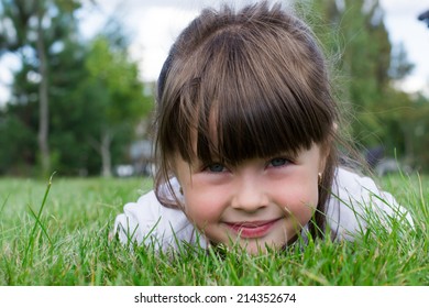 Little Girl Lying On The Grass In The Park, Facing The Camera