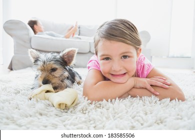 Little girl lying on rug with yorkshire terrier smiling at camera at home in the living room