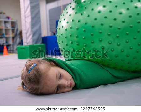 little girl lying in sensory room under fitness ball. Exercising with pressure to help kid relax in a therapy center. sensory integration session
