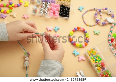Little girl made bracelets on beige background. Kids handmade beaded jewelry. Necklaces and bracelets made from multicolored beads and pearls. DIY bracelet beads.