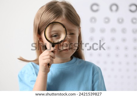 Little girl with magnifying glass against vision test chart