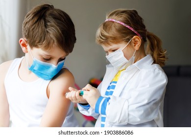 Little Girl Makes Injection To Brother, School Kid Boy. Children, Siblings With Medical Mask Playing Doctor, Holding Syringe With Vaccine. Coronavirus Covid Vaccination Concept. Kids Play Role Game.