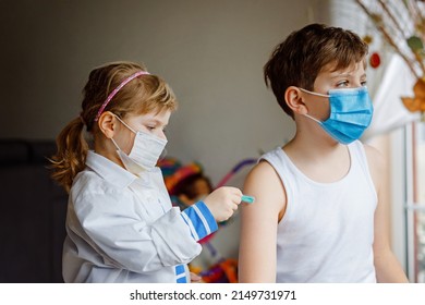 Little girl makes injection to brother, school kid boy. Children, siblings with medical mask playing doctor, holding syringe with vaccine. Coronavirus covid vaccination concept. Kids play role game.