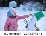 Little girl makes snowman on winter frosty day. Child makes nose out of carrot. . High quality photo