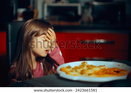 
Little Girl Making a Face palm Gesture at the Dinner Table. Fussy picky eater feeling disappointed in her homemade meal
