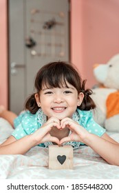 Little Girl Making Sign Heart Gesture By Fingers In Bedroom.