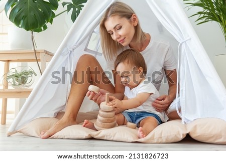 little girl with mamoly plays with a wooden collapsible pyramid for the development of motor skills and thinking while sitting in a wigwam at home