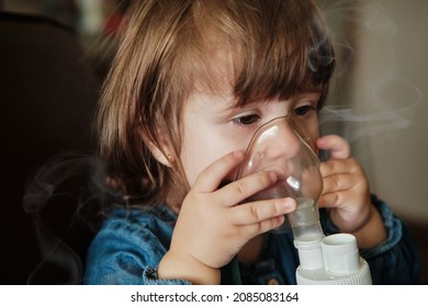 Little girl in a mask, treatments respiratory tract with a nebulizer at home. Baby sits with a nebulizer in his mouth, inhaler, treatment of bronchitis. Nebulizer, cute baby girl using inhaler.
