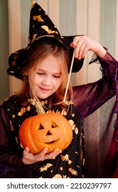 A Little Girl In A Masquerade Witch Costume With A Pumpkin Lantern For Halloween. The Tradition Of Dressing Up And Making Decorations For Halloween.