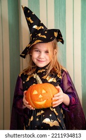 A Little Girl In A Masquerade Witch Costume With A Pumpkin Lantern For Halloween. The Tradition Of Dressing Up And Making Decorations For Halloween.