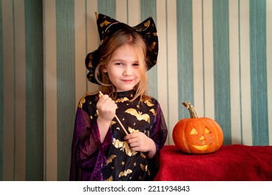 A Little Girl In A Masquerade Witch Costume With A Pumpkin Lantern For Halloween. The Tradition Of Dressing Up And Making Decorations For Halloween.