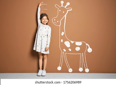 Little girl measuring height   drawing giraffe near brown wall