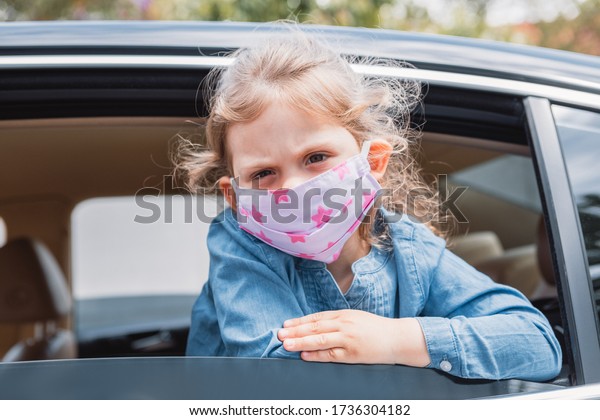 little girl in a medical mask\
from a car window. Hygiene mask protection coronavirus or\
covid-19